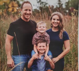 A family with two young sons poses in a field of tall grasses.