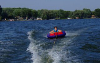A smiling person tubing behind a boat on Lake Winnebago, enjoying the sunny weather and calm water.