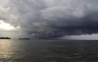 A dramatic storm cloud approaches over Lake Winnebago near Garlic Island, casting shadows across the lake under a turbulent sky.