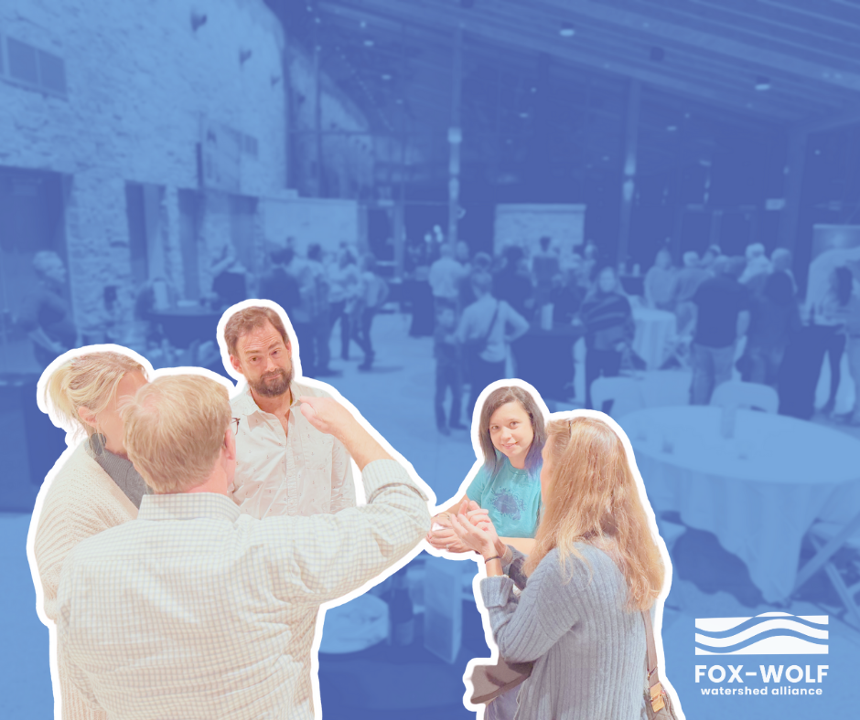 A small group shares an animated discussion in the foreground of the 2024 Happiest Hour, while dozens of attendees mingle in the blue-tinted background of the event space.