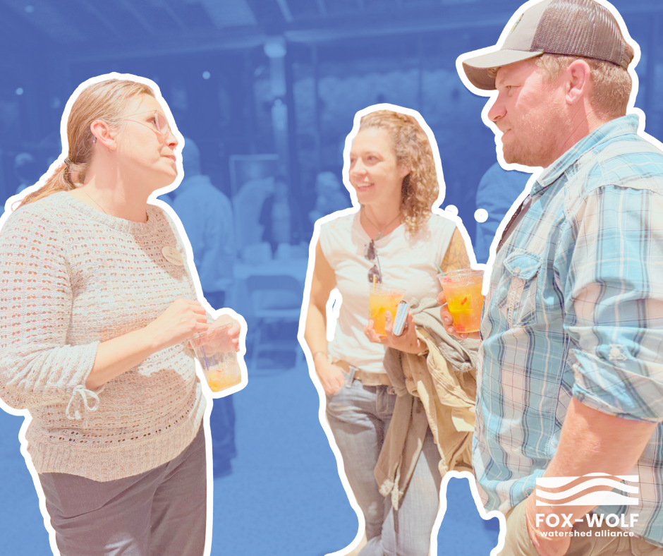 Three attendees chat casually with drinks in hand at the 2024 Happiest Hour. The celebratory atmosphere shines through as they smile and connect in front of the softly lit, blue-toned crowd behind them.