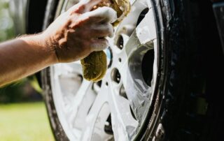 Person scrubbing a car tire with a soapy sponge on a grassy lawn