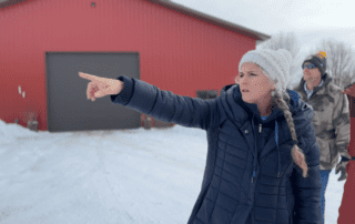 Shelly Christie gestures toward snow-covered farmland near a red barn in Waushara County as others look on.