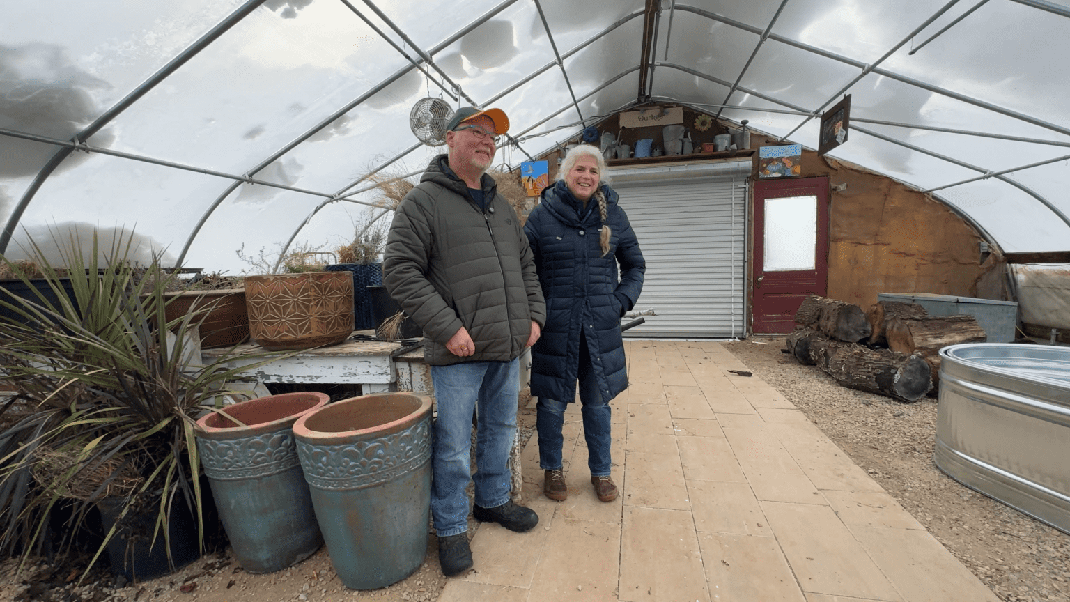Scott and Shelly Christie stand inside their Waushara County greenhouse surrounded by potted plants and garden tools.