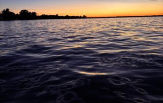 A low-angle view of Lake Winnebago at sunrise, the sky shifting from deep blue to orange above a calm, textured surface